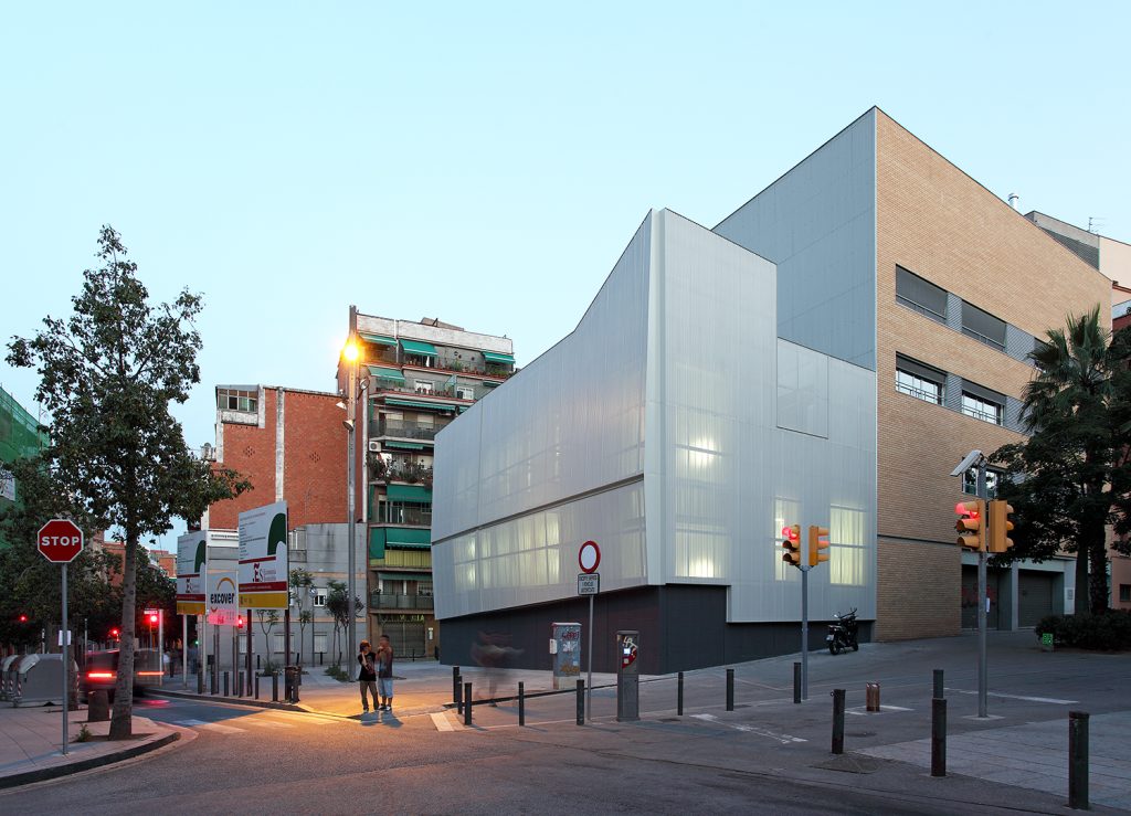 Social Service Center in Prosperitat - Conxita Balcells - Minimalist gray building with lights in the interior seen from the sidewalk