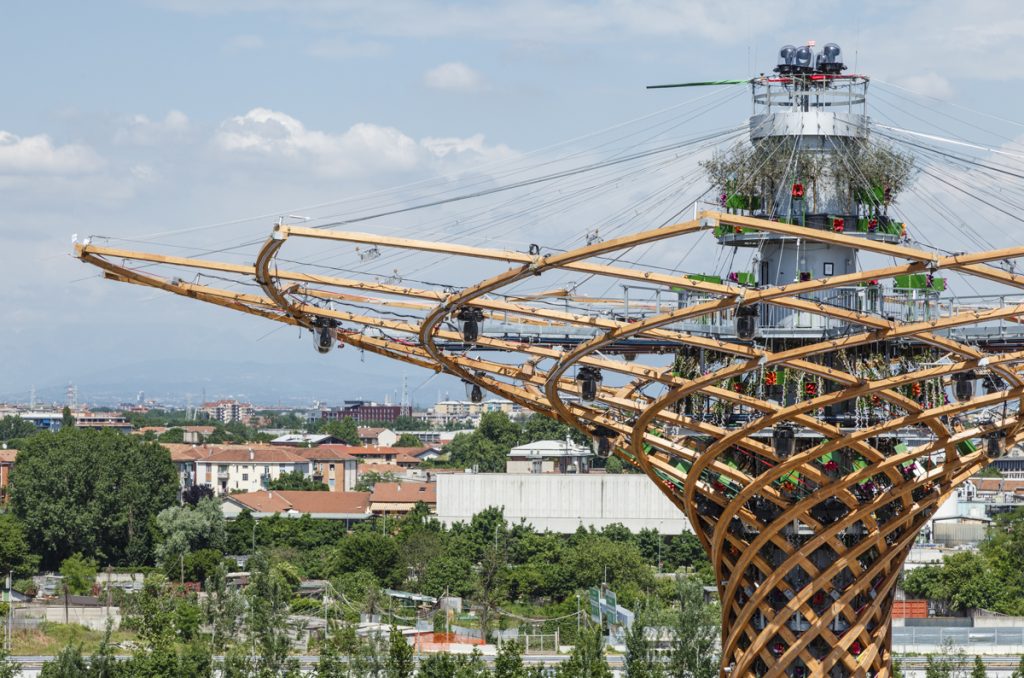Expo Milan 2015 - Various - Colossal wooden lattice structure with outstretched arms stands amid a serene cityscape