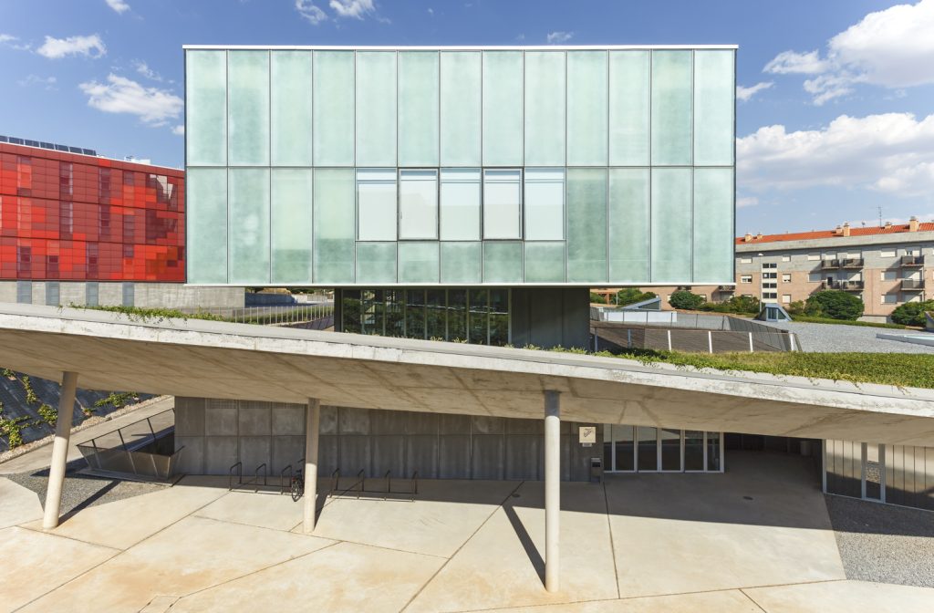 Institute of Neuroscience of Castilla y León - Mapaac Arquitectos - Modern building with a greenish glass facade is elevated on pillars
