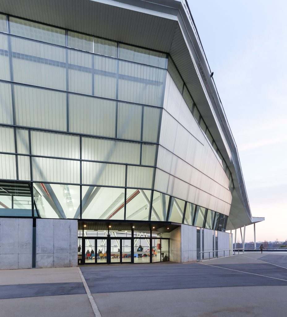 Indoor Athletic Stadium - Mario Corea Lluis Moran - Modern glass building at dusk, showcasing a sleek design with illuminated interiors