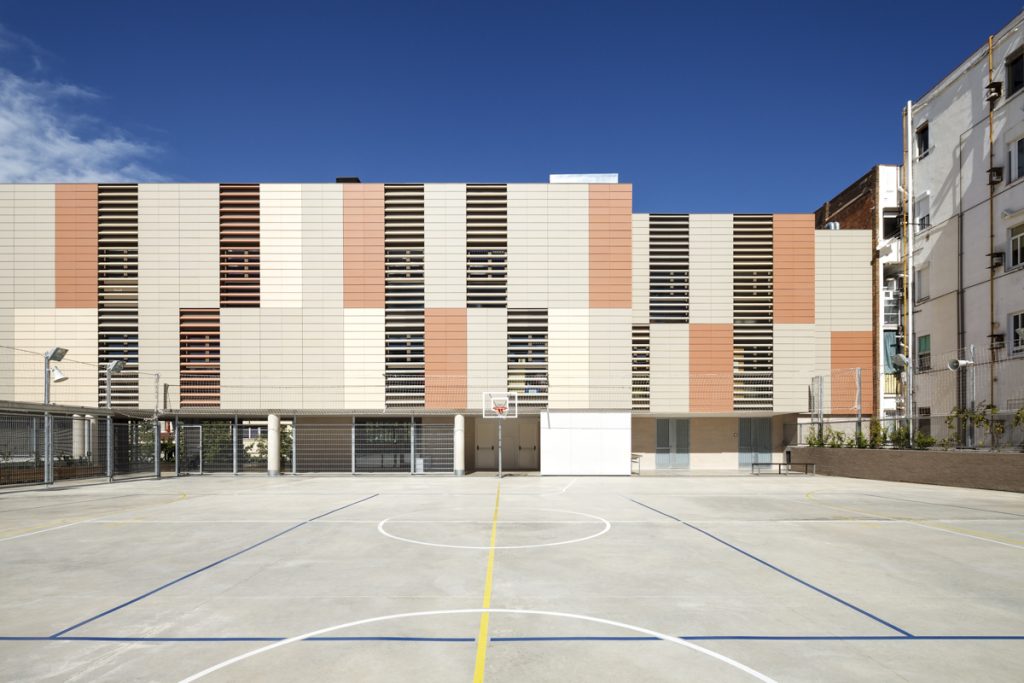 Univers School - ONL arquitectura - Empty basketball court with a modern, patterned building in the background under a clear blue sky